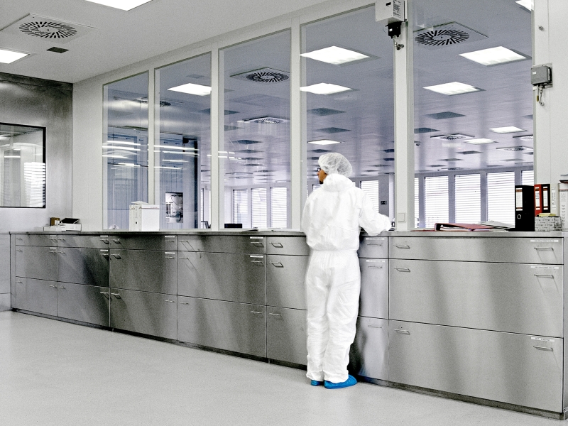 In weiß gekleideter Labor-Mitarbeiter arbeitend vor Edelstahl-Pharma-Mlöbel mit Sonderhöhe