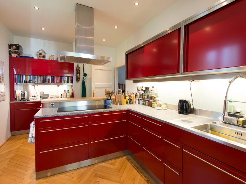 Design-Küche in Edelstahl mit rot pulverbeschichteten Flächen und Niro-Griffen; Abdeckung ist eine Kombination aus Stein- und Edelstahlplatte mit fugenlosem Wandhochzug und fugenlos eingeschweißtem Waschbecken